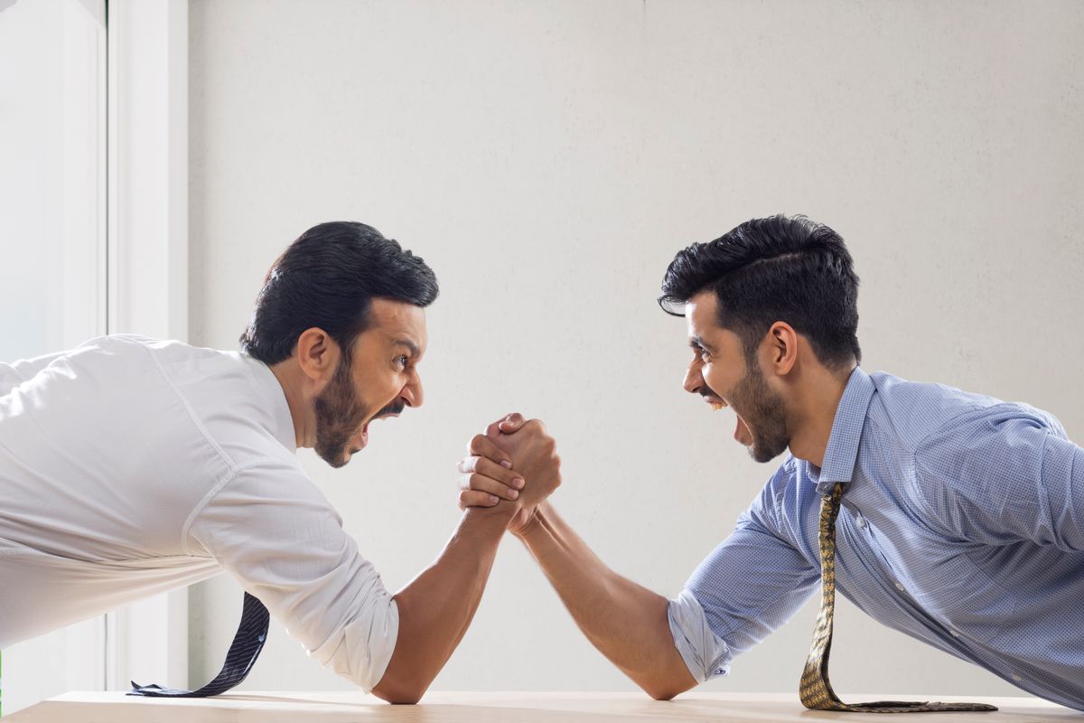Corporate employees in formal clothing engaged in an arm wrestling match.
